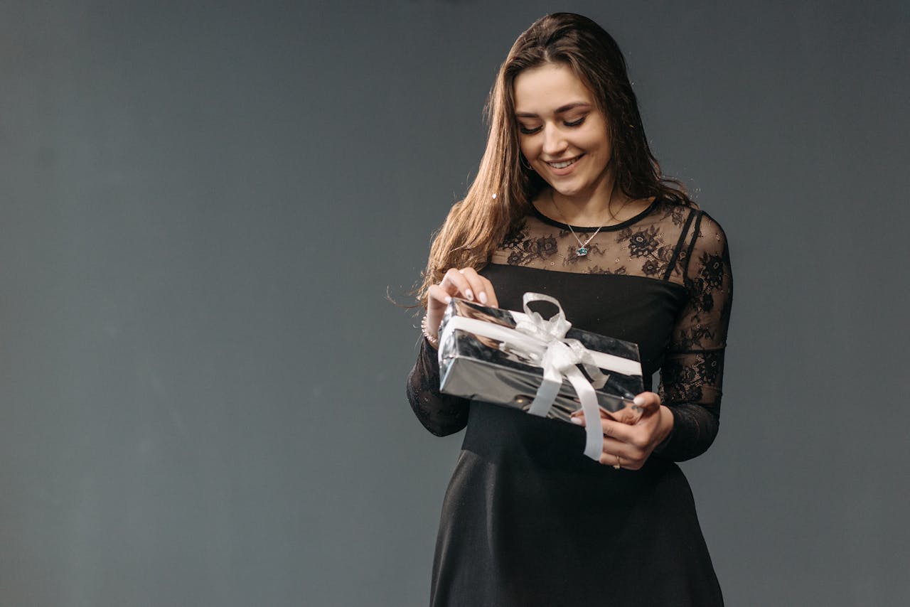 Femme en robe élégante ouvrant un cadeau avec ruban — idée cadeau original pour femme