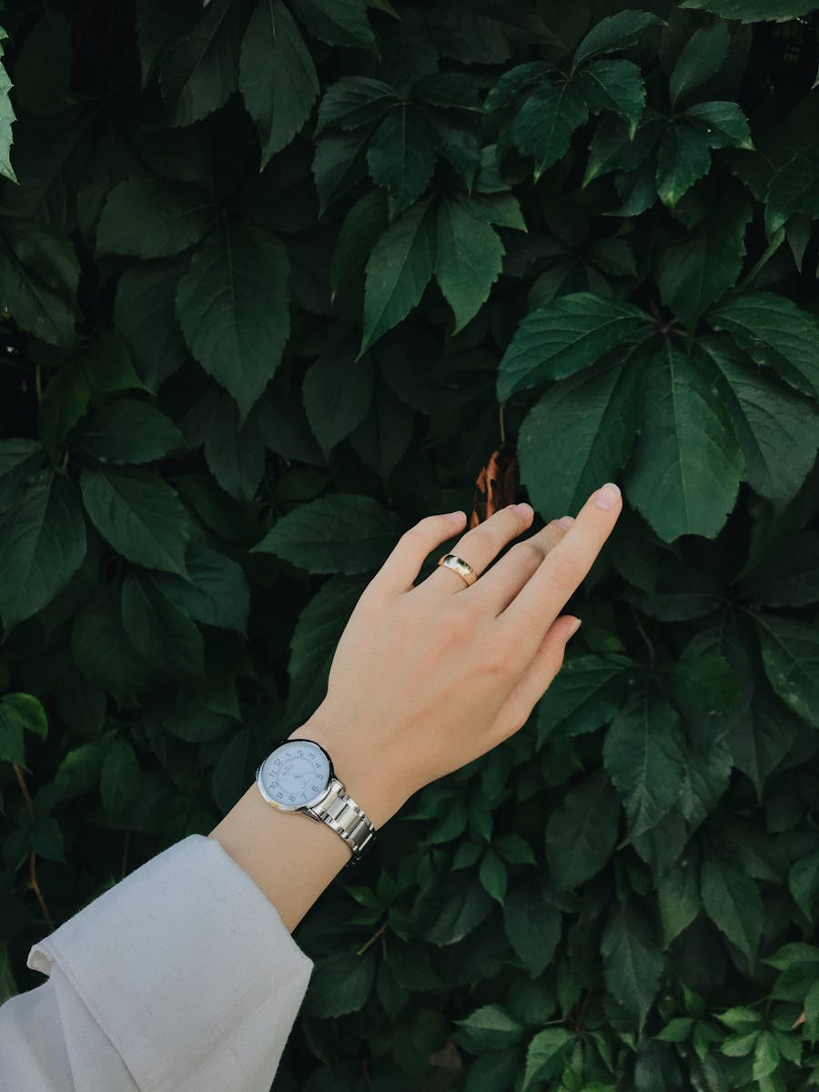 Main féminine portant une montre au poignet, touchant des feuilles vertes — montre femme écoresponsable