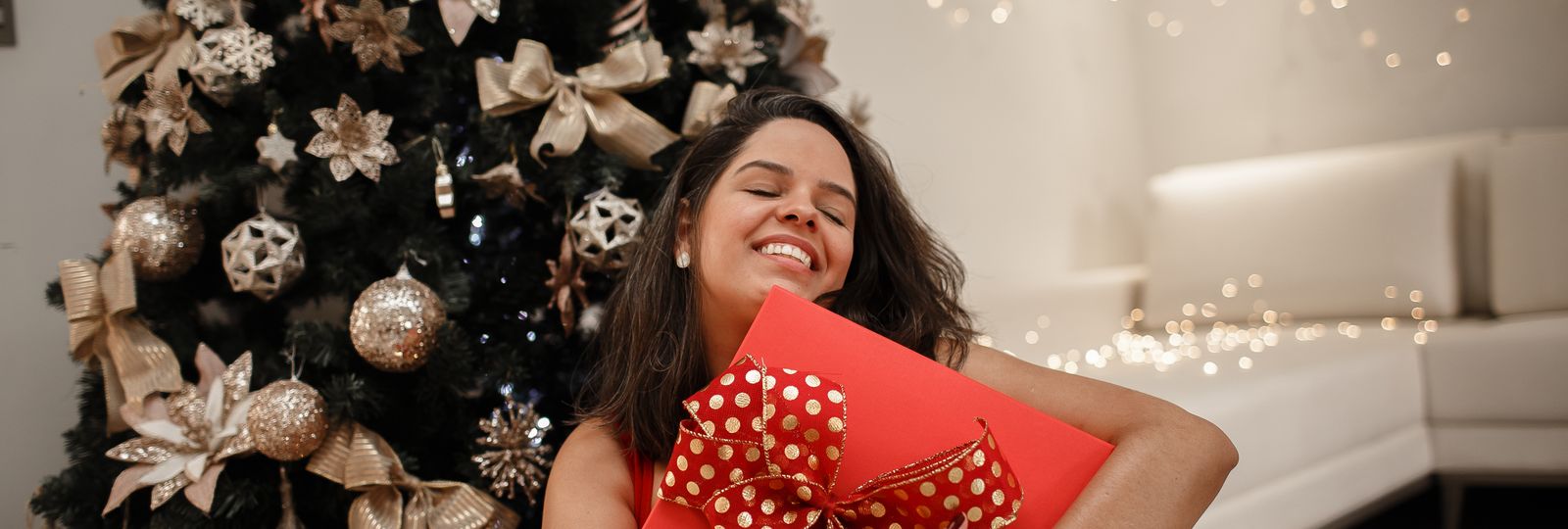 Cadeau de Noël montre — femme souriante tenant un cadeau devant un sapin décoré