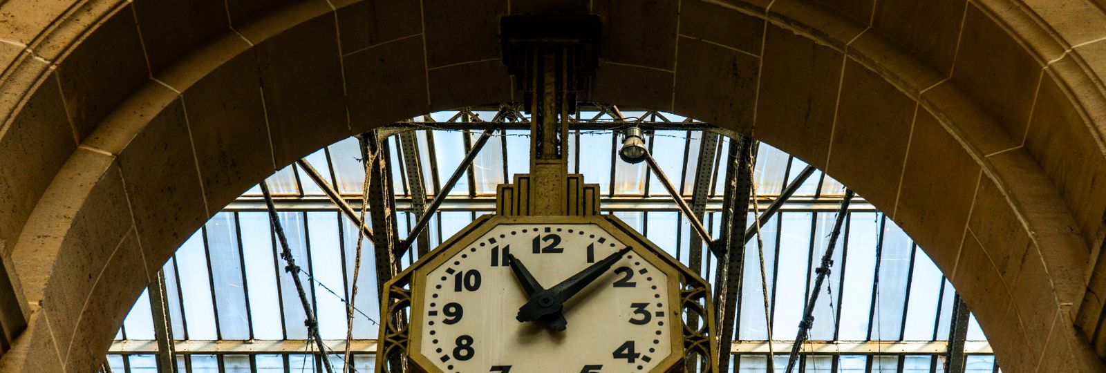 Grande horloge de gare ancienne suspendue sous une verrière métallique