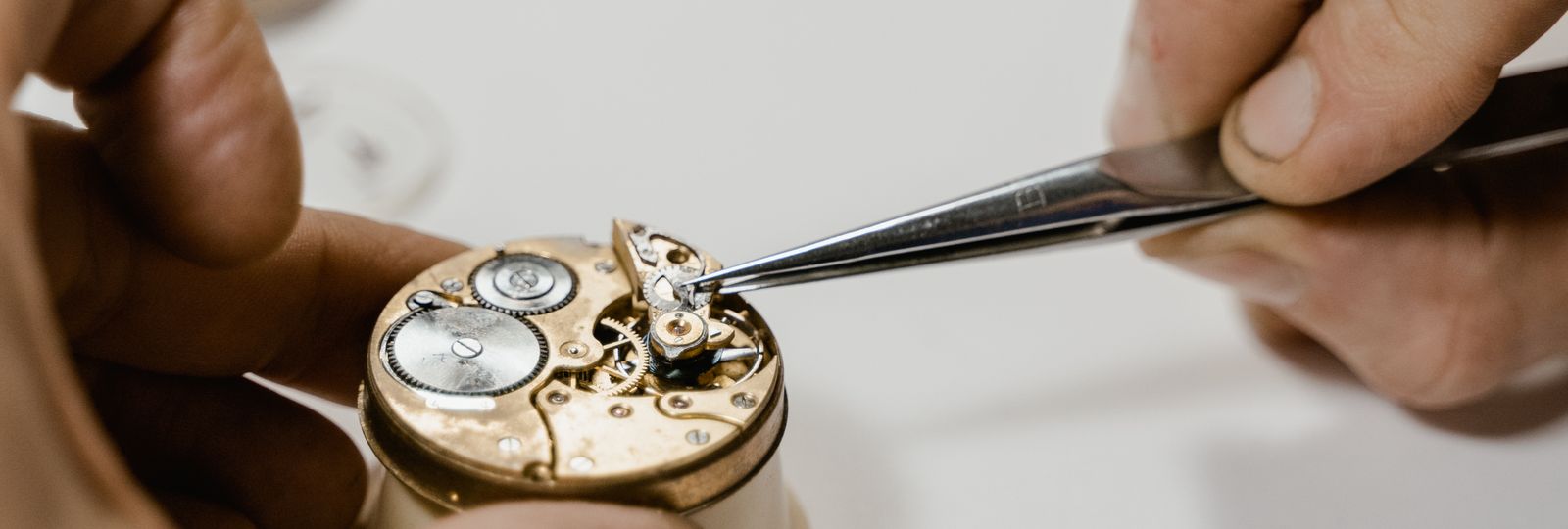 Mains d'horloger manipulant à la pince les rouages d'un mouvement mécanique ouvert